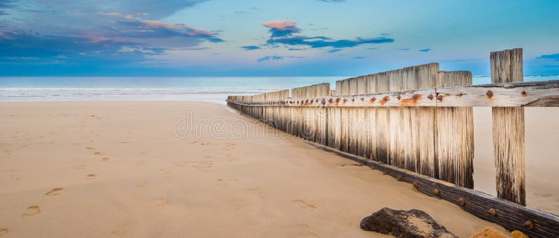 Wooden fence on empty beach at sunset