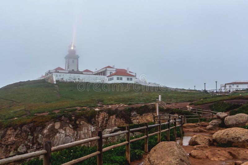 Wooden fence puddle and luminous lighthouse at Cape Roca