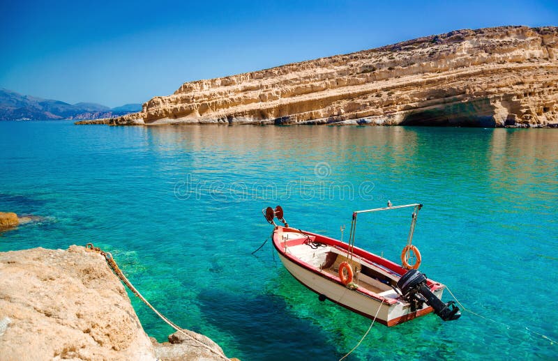 Wooden fishing boats at Matala beach with caves on the rocks, Crete, Greece.