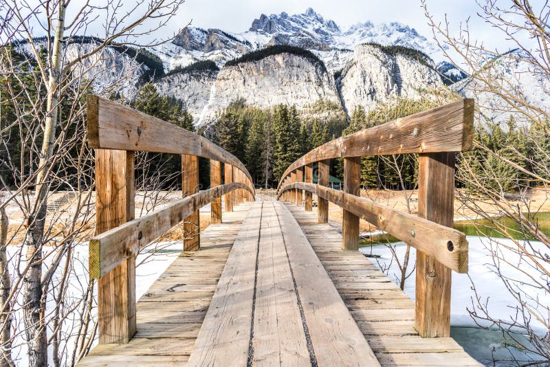 Wooden foot bridge leading over glacial stream to inspiring winter mountains landscape