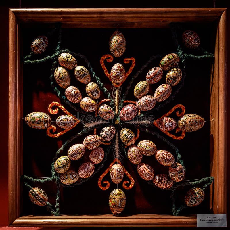 A wooden frame with a cluster of colorful eggs in the center. The eggs are arranged in a circular pattern, with some of them overlapping each other. The frame is made of wood