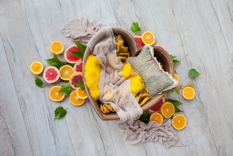 Wooden heart with yellow props and a pillow for photographing a baby, decorated with oranges, grapefruit and green leaves