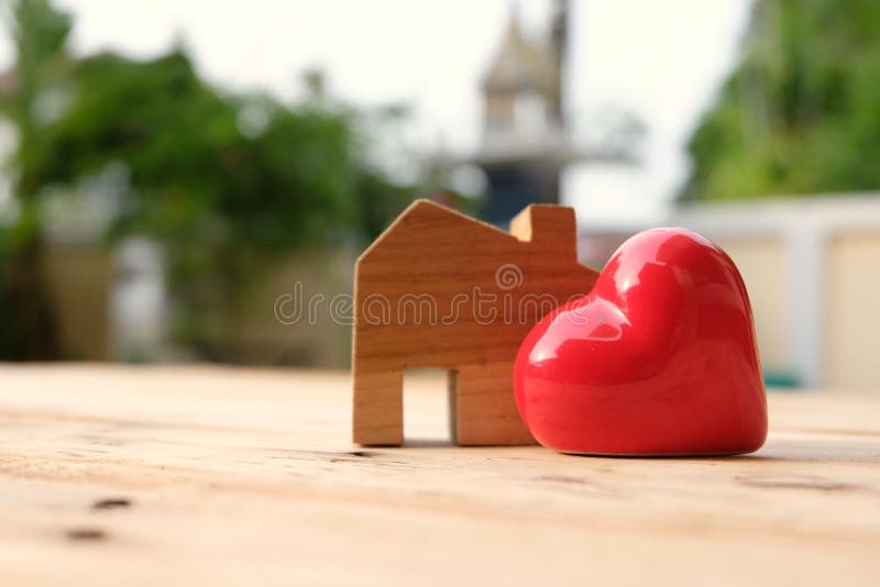 Wooden house model stand aside of big red heart. Happy home and family concept. Love concept