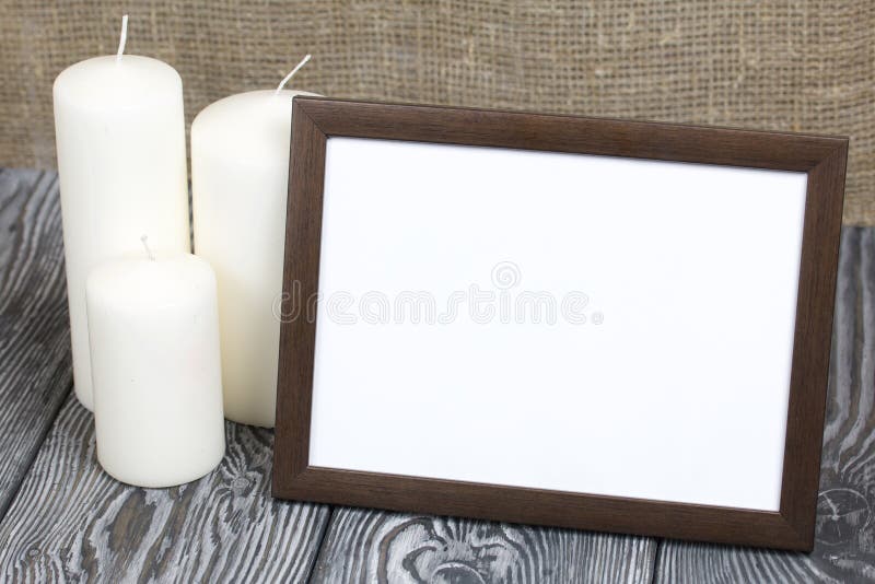 Wooden photo frame with a white field for an inscription or a picture. There are candles nearby royalty free stock photography