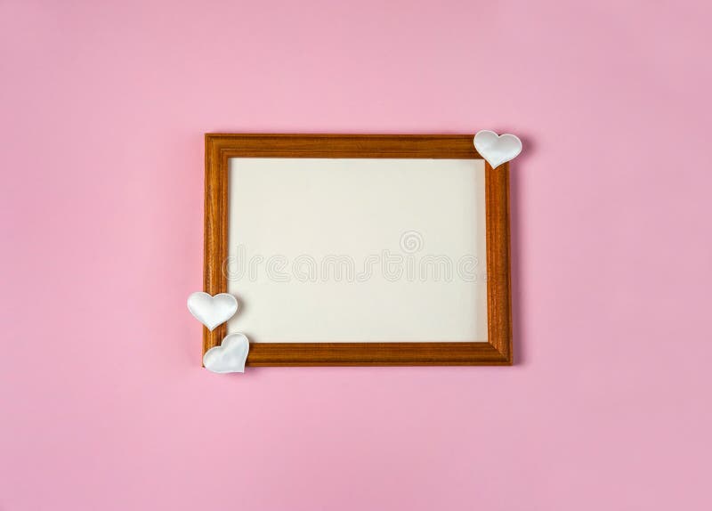 Wooden photo frame and white hearts on pink background.