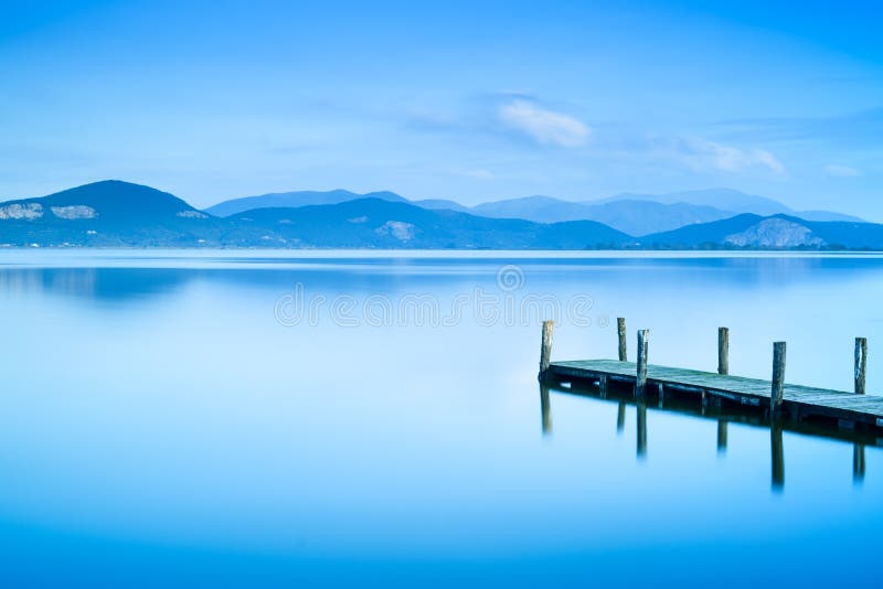 Wooden pier or jetty and on a blue lake sunset and sky reflection on water. Versilia Tuscany, Italy