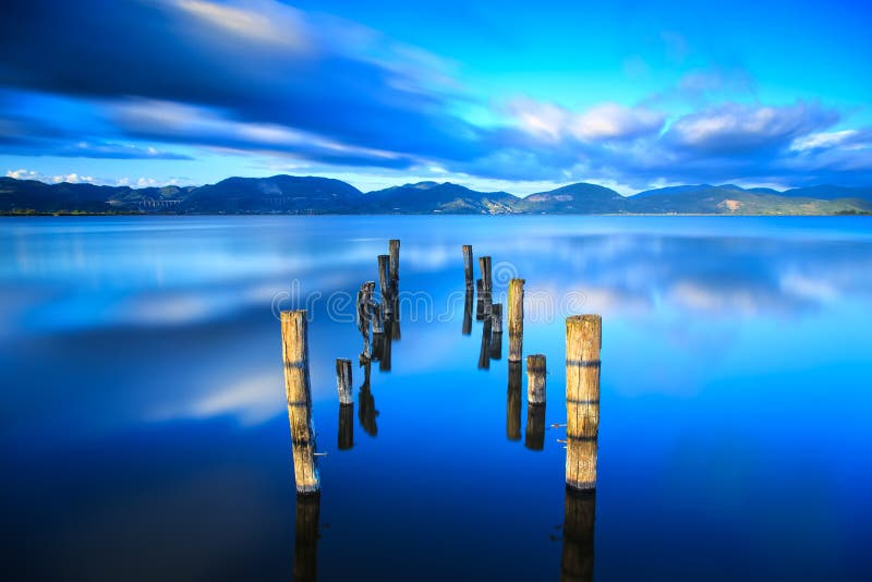 Wooden pier or jetty remains on a blue lake sunset and sky reflection on water. Versilia Tuscany, Italy