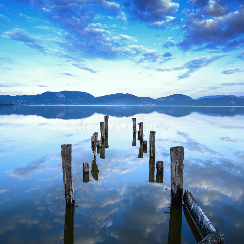 Wooden pier or jetty remains on a blue lake sunset and sky reflection on water. Versilia Tuscany, Italy