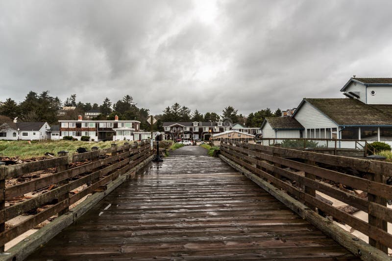 A wooden pier in Siletz Bay along the coast against houses in Oregon, USA on a cloudy day