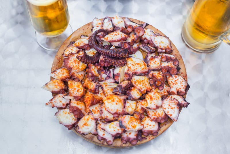Wooden plate of galician style cooked octopus with paprika and olive oil and Glasses of cold Beer. royalty free stock image