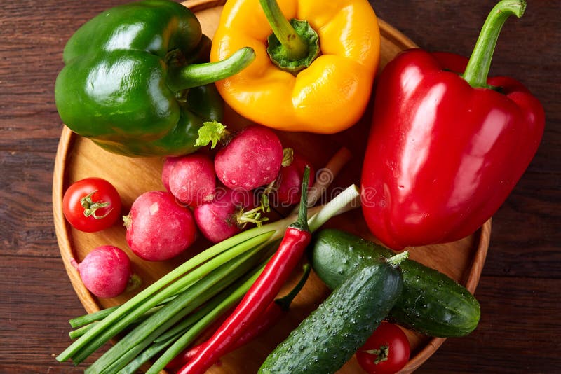 Wooden plate with vegetables for a vegetarian salad on rustic wooden background, close-up, selective focus