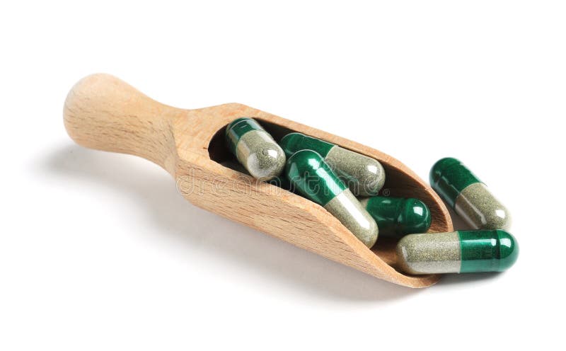 Wooden scoop with green spirulina capsules on white