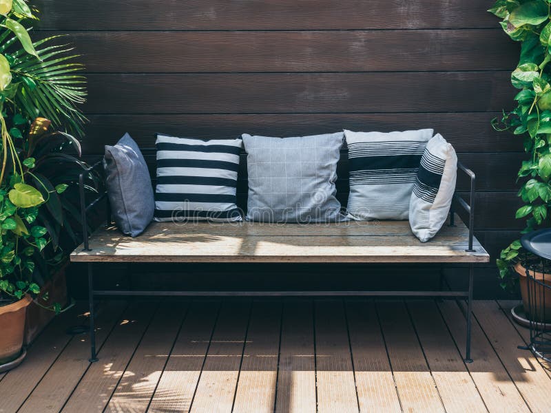 Wooden sofa with pillows between green tropical trees in terra cotta pots on wooden wall background