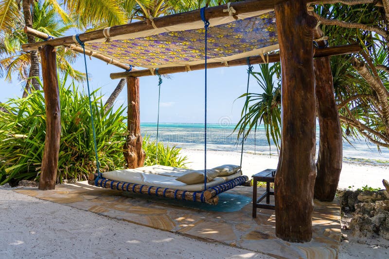 Wooden swing with a mattress and pillows under a canopy on the tropical beach near sea, island Zanzibar, Tanzania, East Africa