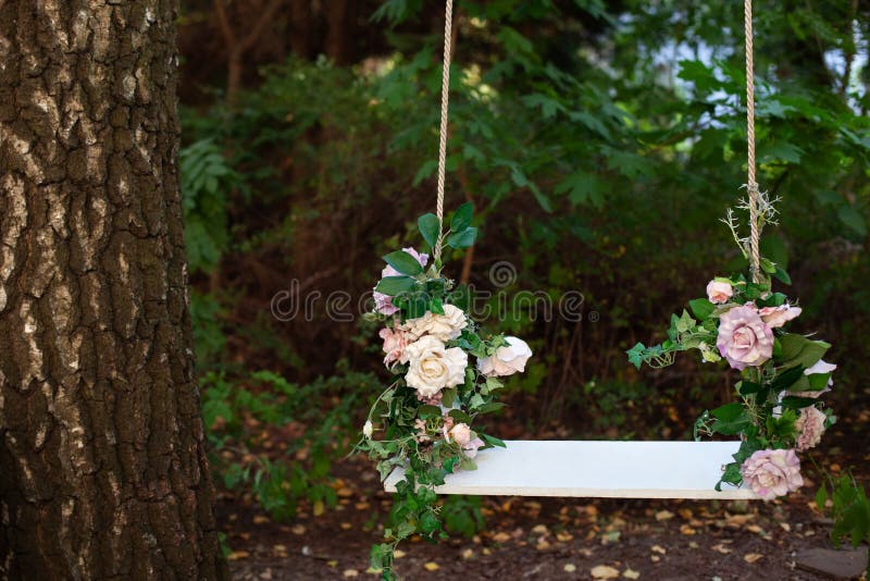 Wooden swing in playground outdoors. Empty swing placed in park. Wedding swing decorated with flowers roses. Garden swing hanging