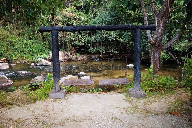 Wooden swing set beside a stream and relaxing atmosphere.