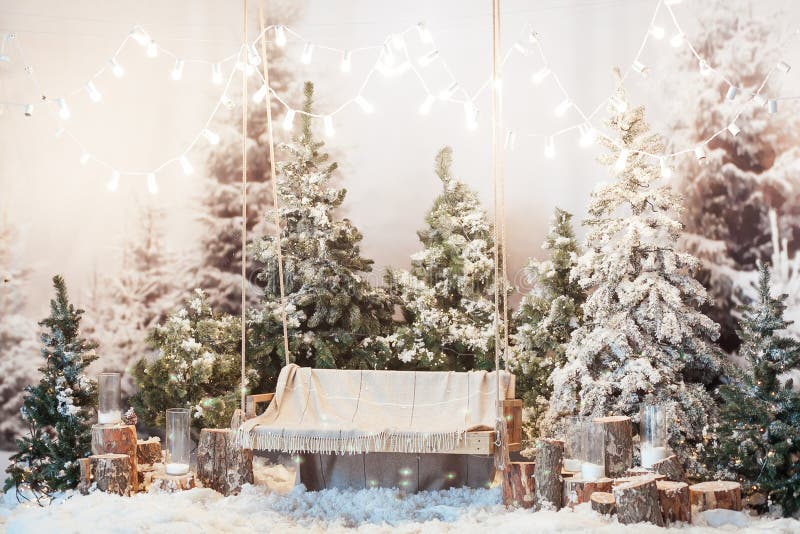 Wooden swing in a snow-covered park or forest with spruce trees and stumps, big candles in glass vases, while snowing