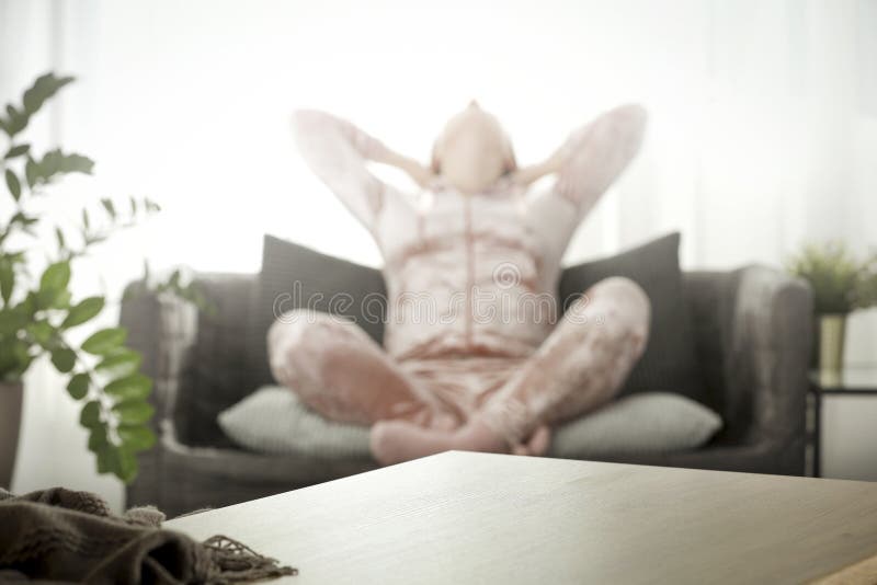 Wooden table top with blurred background of woman sitting on the sofa and morning time in nice cozy home interior