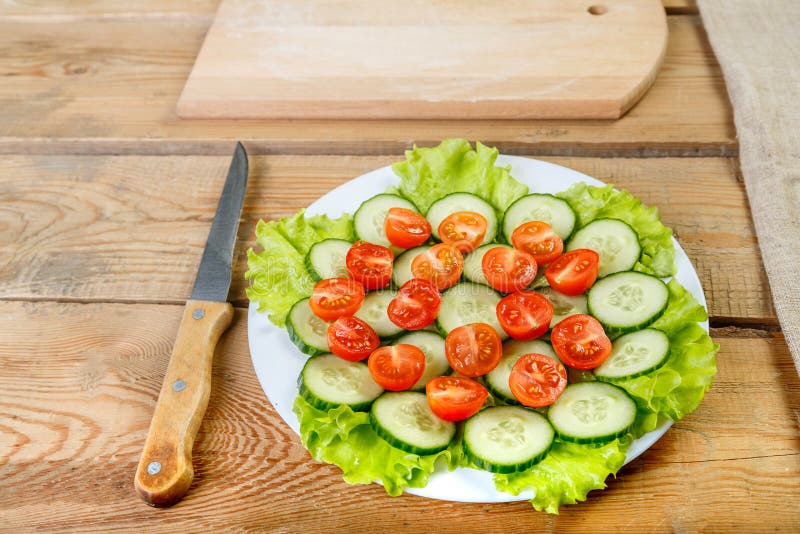 A wooden table on a white plate is sliced cucumbers, tomatoes