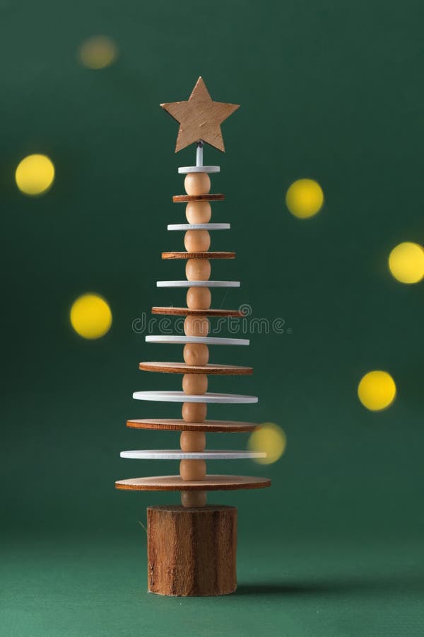 Wooden toy in the shape of Christmas tree with the star on top. Dark green festive background with warm bokeh blurred lights. Close-up.