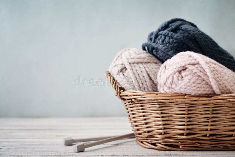 Wool yarn in coils with knitting needles in wicker basket on light blue background