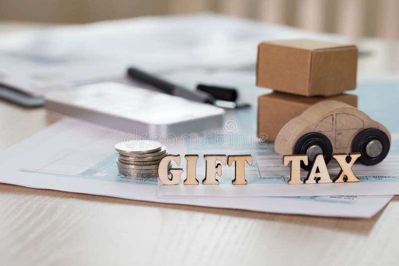 Word GIFT TAX composed of wooden letters. Coins, papers, pen, wooden car, carton boxes in the background. Closeup royalty free stock image
