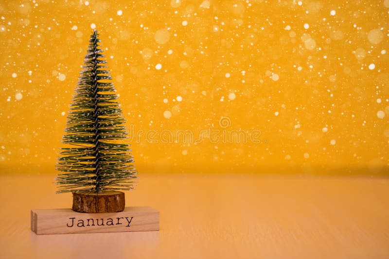 Word `January` on wodden table with christmas tree and yellow background