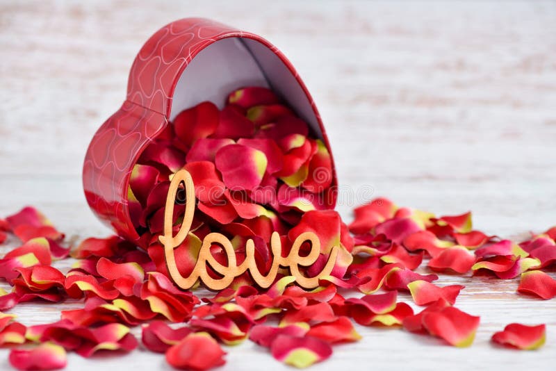 The word `Love` on a background of red rose petals falling out of a heart-shaped box