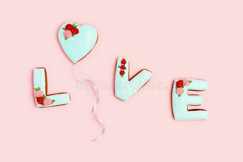 Word Love from homemade ginger biscuits and one in form heart flying as balloon, pink background. Valentines day. Holiday sweet food concept. Pastel colors