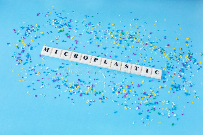 Word MICROPLASTIC around small plastic particles on a blue background. Microplastic in water and food