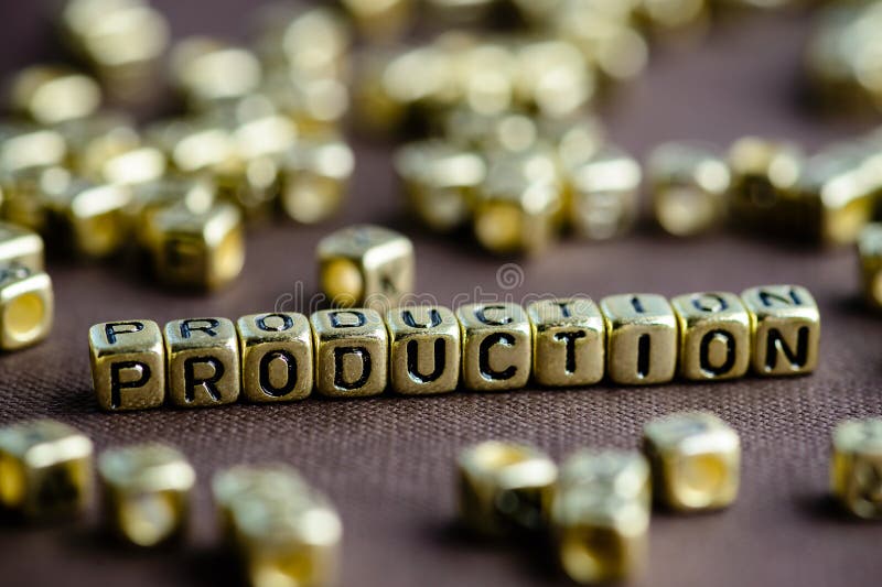 Word PRODUCTION made from small golden letters on the brown background, selective focus. Business concept background