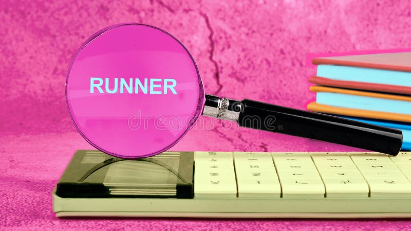 The word RUNNER through a magnifying glass placed on a calculator, and next to it - a stack of colorful books on a bright pink stock image