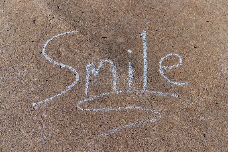 The word Smile written with sidewalk chalk on gray concrete pavement background