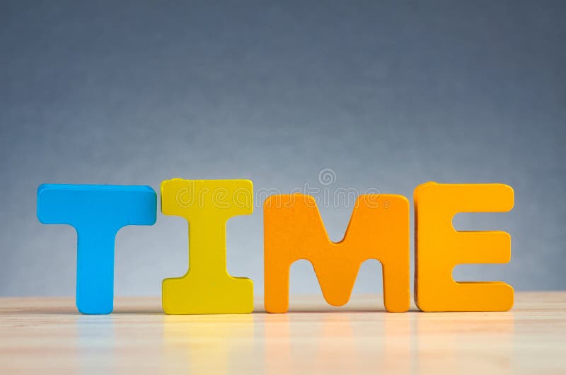 Word TIME spelled using wooden alphabet on desk over gently lit dark background