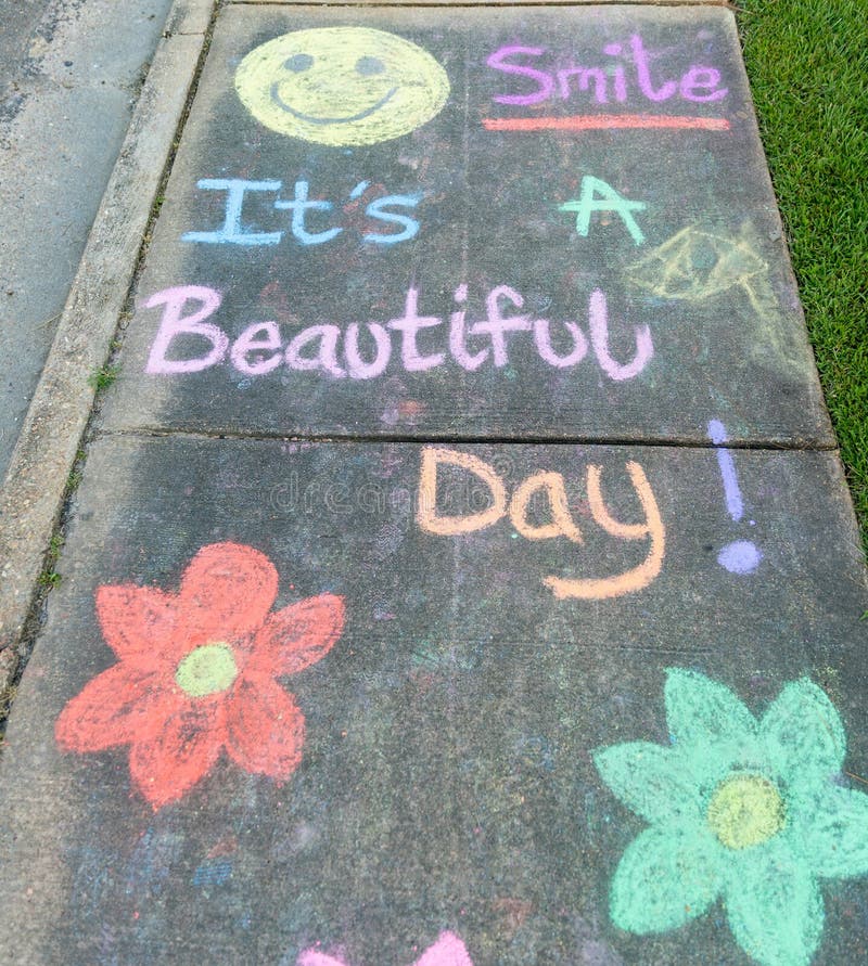 The words &#x22;Smile It&#x27;s a Beautiful Day&#x22; written with sidewalk chalk on gray concrete pavement background. The words &#x22;Smile It&#x27;s a Beautiful Day&#x22; written with sidewalk chalk on gray concrete pavement background