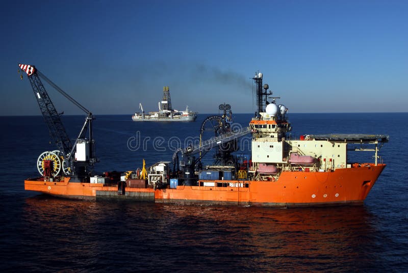 A large boat spools out umbilical control cable as part of a deepwater well completion, while a drillship completes another well for eventual production. A large boat spools out umbilical control cable as part of a deepwater well completion, while a drillship completes another well for eventual production.