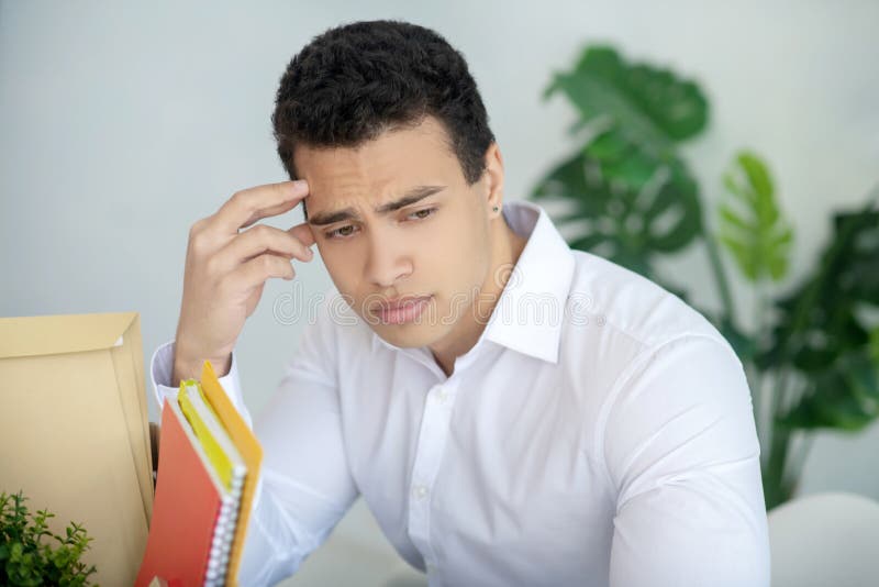Depressed brunette male sitting at his desk, touching his forehead royalty free stock photography Depressed brunette male sitting at his desk, touching his forehead royalty free stock photography