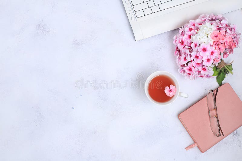 Work desk of a modern woman, home office. Notepad, tea, spring flowers on a light table. Minimal business concept, flat lay