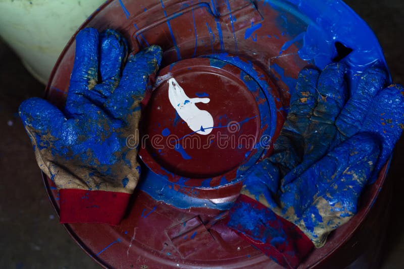 Gloves Stained with Blue Paint Lie on a Red Barrel Filled with Blue