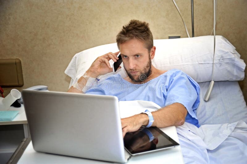 Workaholic business man in hospital room lying in bed sick and injured working with mobile phone computer laptop