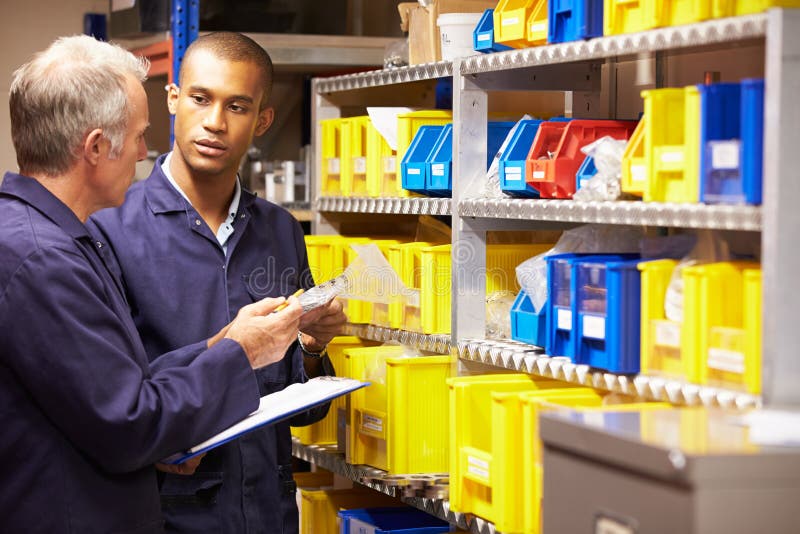 Worker And Apprentice Checking Stock Levels In Store Room