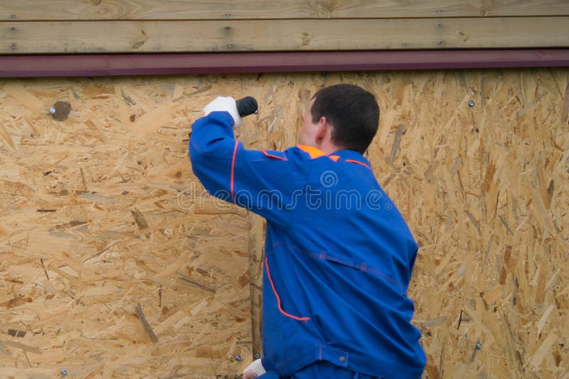 A worker in a blue uniform drills wooden boards in the lower part of the house royalty free stock photo A worker in a blue uniform drills wooden boards in the lower part of the house royalty free stock photo
