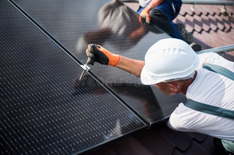 Worker building photovoltaic solar panel system on rooftop of house with help of hex key. royalty free stock photo