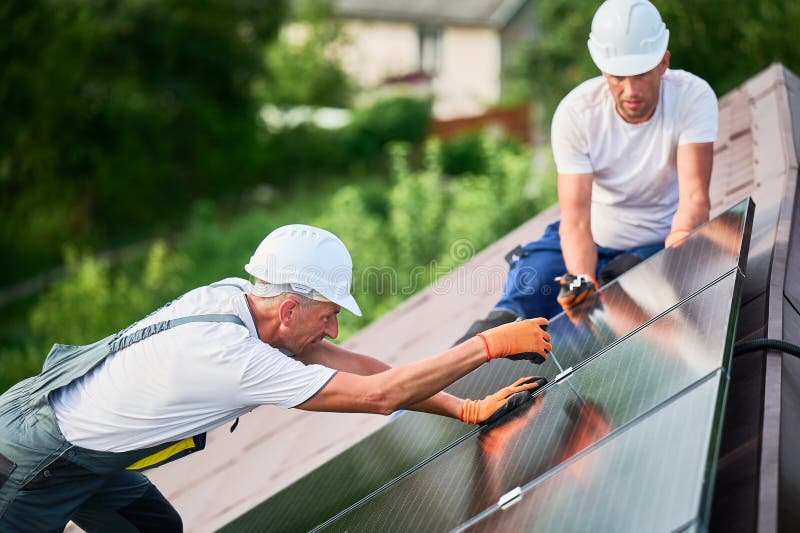 Worker building photovoltaic solar panel system on rooftop of house with help of hex key. royalty free stock image