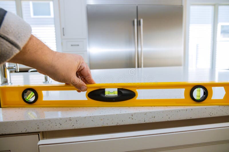 A worker checks the leveling of a granite countertops in a home kitchen remodel, renovation, measurement, stone, measuring, construction, industry, equipment, repair, man, tool, handyman, interior, service, sink, improvement, installation, craftsman, professional, decoration, contemporary, male, installing, modern, builder, designer, material, cabinet, furniture, working, skill, built-in, repairman, manual, building, contractor, instruments. A worker checks the leveling of a granite countertops in a home kitchen remodel, renovation, measurement, stone, measuring, construction, industry, equipment, repair, man, tool, handyman, interior, service, sink, improvement, installation, craftsman, professional, decoration, contemporary, male, installing, modern, builder, designer, material, cabinet, furniture, working, skill, built-in, repairman, manual, building, contractor, instruments