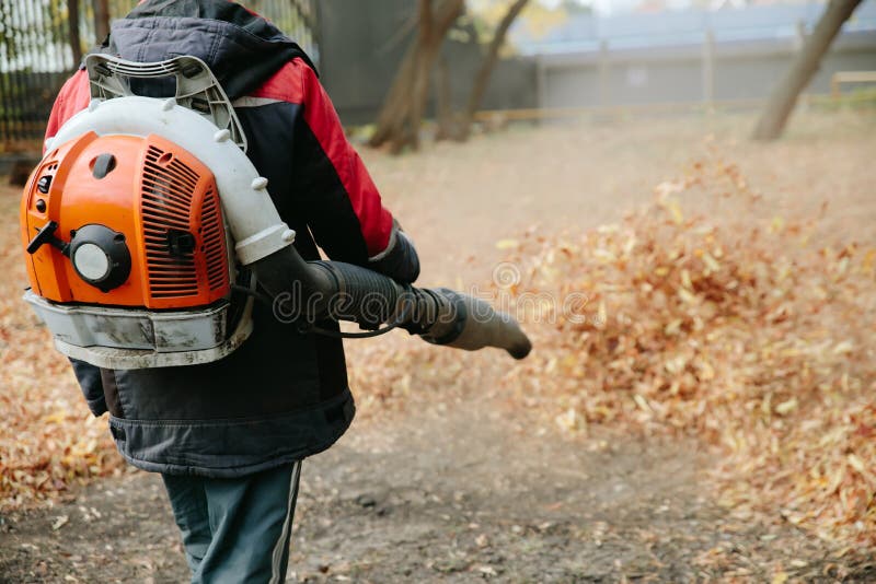 Worker Cleaning Lawn in Park from Dead Leaves Using Gas Powered Leaf
