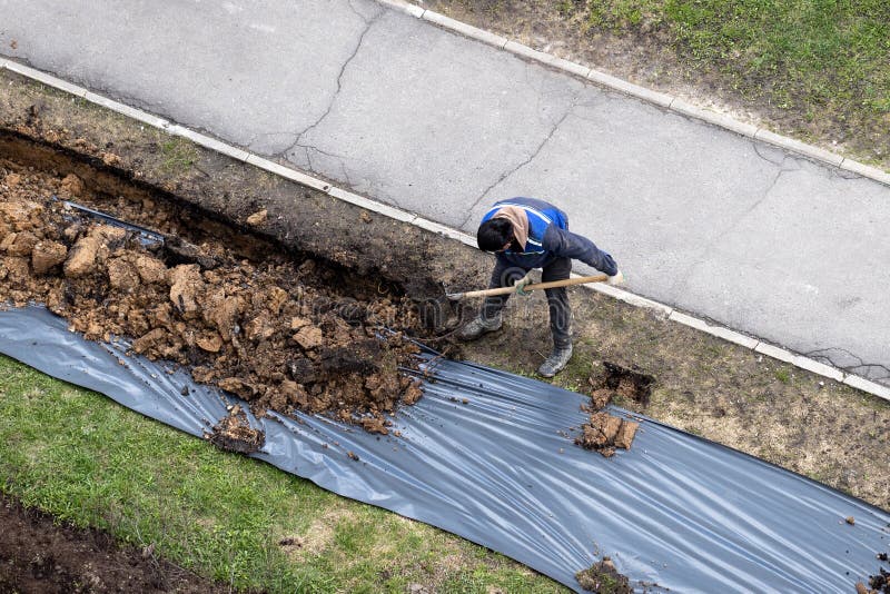 A worker digging a ditch along a pavement in summer. royalty free stock photo