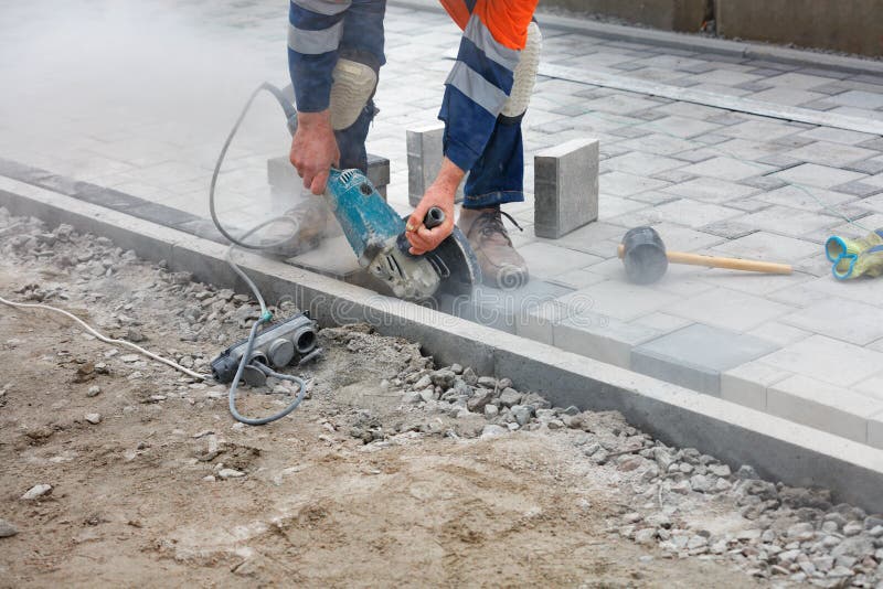 A Worker with an Electric Grinder Cuts Paving Slabs at a Construction Site Stock Photo Image