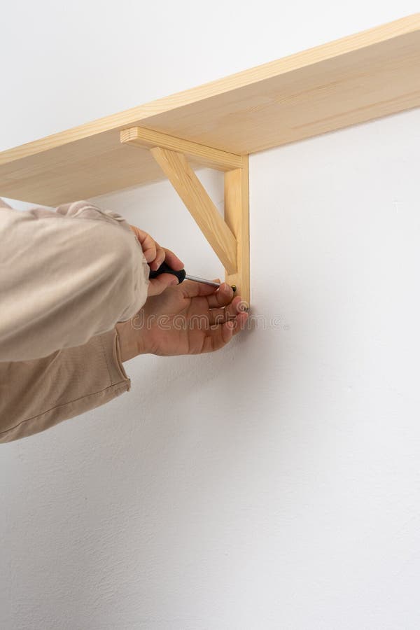 A Worker Fixes Screws on a Shelf Corner with a Screwdriver Stock Photo