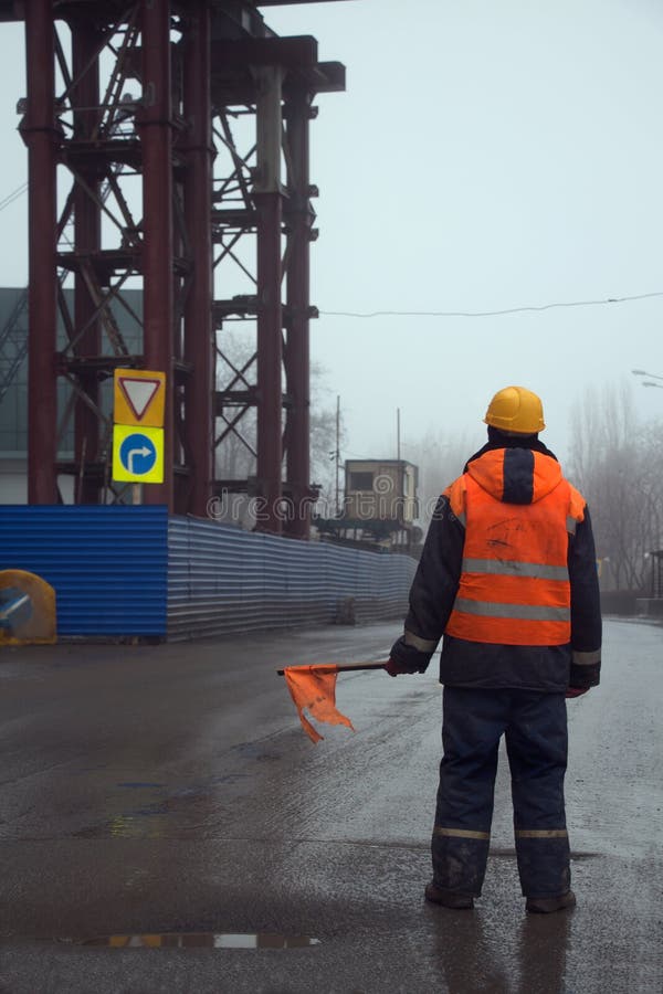Worker with Flag Standing Across the Road Preventing Traffic in